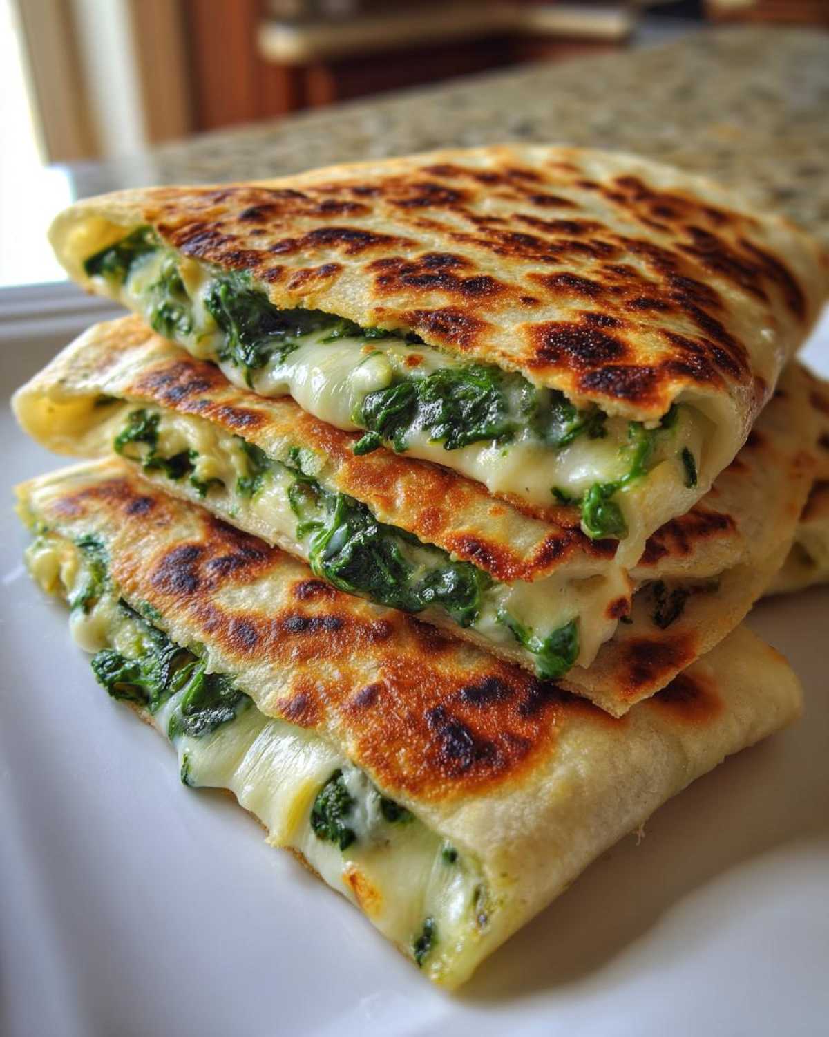 Close-up of stacked Creamy Spinach Artichoke Quesadillas showing melted cheese oozing out with spinach.