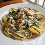 A close-up of a white bowl filled with Creamy Spinach Chicken Pasta with Alfredo Sauce, topped with grilled chicken pieces.