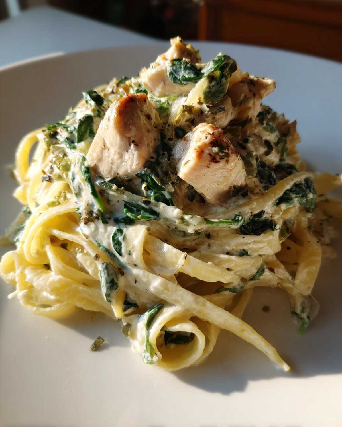 Close-up of a serving of Creamy Spinach Chicken Pasta with Alfredo Sauce, featuring fettuccine, chunks of chicken, and wilted spinach.