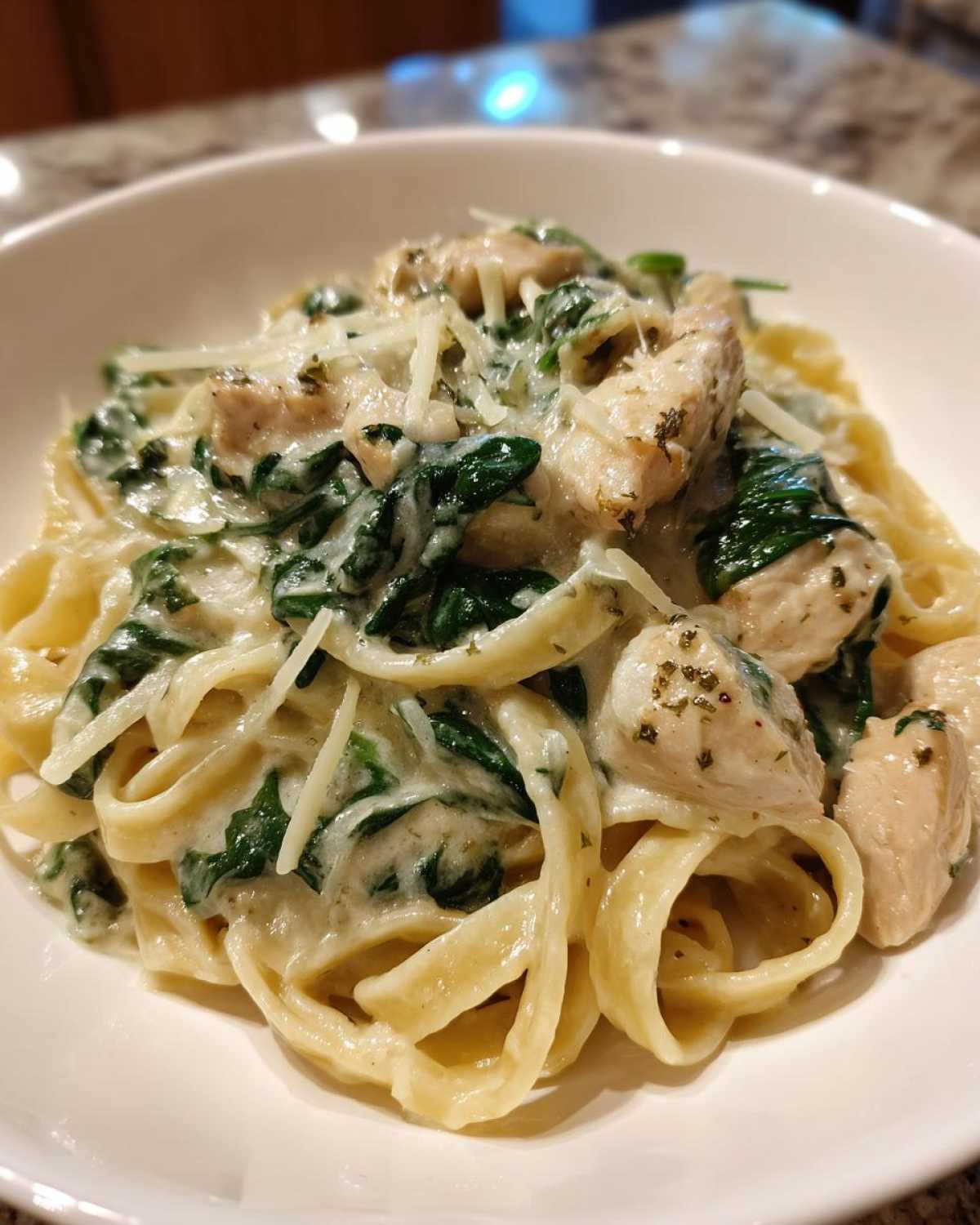 Close-up of a bowl filled with fettuccine pasta, chunks of chicken, spinach, and creamy sauce, topped with grated cheese for a Creamy Spinach Pasta with Chicken Dinner.