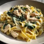 A bowl filled with fettuccine noodles tossed in a rich, creamy sauce with wilted spinach and chunks of seasoned chicken, perfect for a Creamy Spinach Pasta with Chicken Dinner.