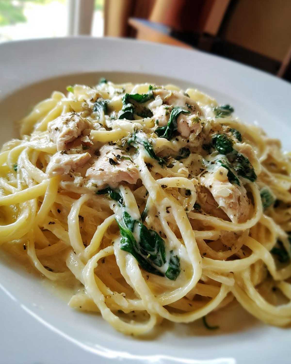 A close-up view of a serving of Creamy Spinach Pasta with Chicken Dinner, featuring linguine coated in a rich white sauce with chunks of chicken and wilted spinach.