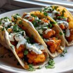 Three Crispy Chicken Tacos topped with white sauce and cilantro, ready to eat.