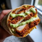 A cross-section view of a Crispy Chicken Wrap with Avocado Sauce, showing layers of breaded chicken and green sauce.
