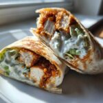 Two halves of a Crispy Chicken Wrap with Creamy Garlic Sauce, showing crispy chicken, lettuce, and white sauce inside a toasted tortilla.