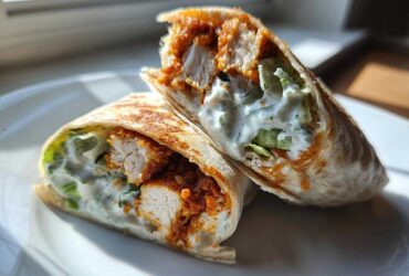 Two halves of a Crispy Chicken Wrap with Creamy Garlic Sauce, showing crispy chicken, lettuce, and white sauce inside a toasted tortilla.