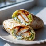 A close-up of a Crispy Chicken Wrap with Creamy Ranch Sauce cut in half, showing crispy chicken, lettuce, and sauce.