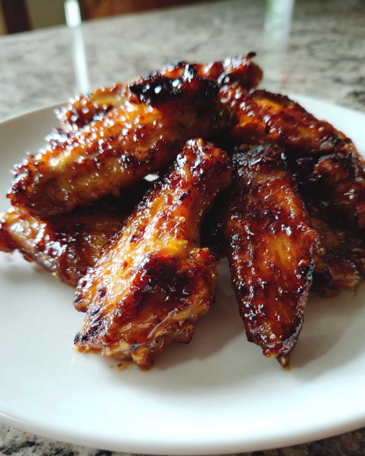 Close-up of several glossy, caramelized Honey Garlic Chicken Wings Crispy Oven Baked piled on a white plate.
