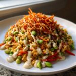 A mound of Crispy rice salad with edamame, shredded carrots, and a generous drizzle of creamy tahini ginger dressing.