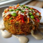 A perfectly molded, crispy rice salad patty topped with shredded carrots, edamame, and drizzled with creamy tahini ginger dressing.
