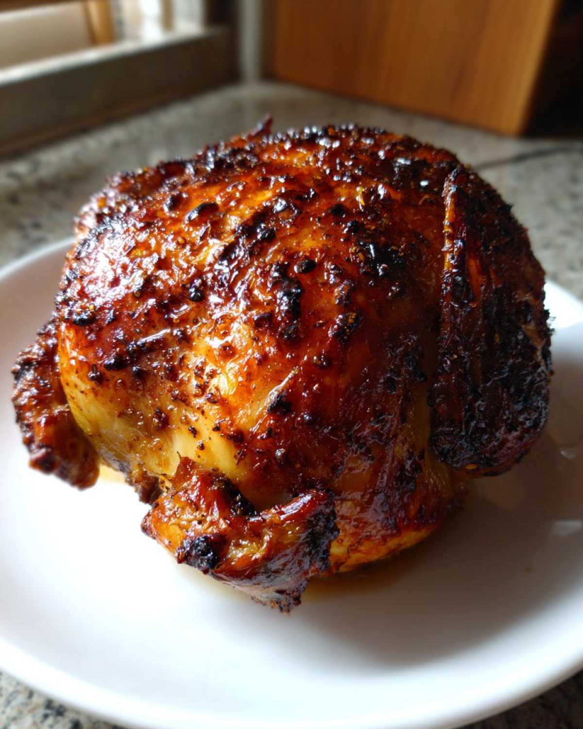 A whole roasted chicken with incredibly crispy, dark golden-brown skin, served on a white plate, showcasing the Lemon Herb Roasted Chicken.