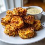 A stack of golden brown, crispy Delicious Air Fryer Fried Pickles served on a white plate next to a small bowl of dipping sauce.