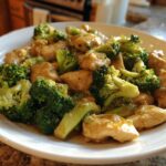 A white plate filled with pieces of tender chicken and bright green broccoli florets coated in a savory Garlic Butter Chicken and Broccoli Stir Fry sauce.