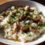 A close-up of a white bowl filled with fluffy white rice topped with chunks of chicken and fresh parsley, representing the Garlic Butter Chicken and Rice One Pot Dinner.