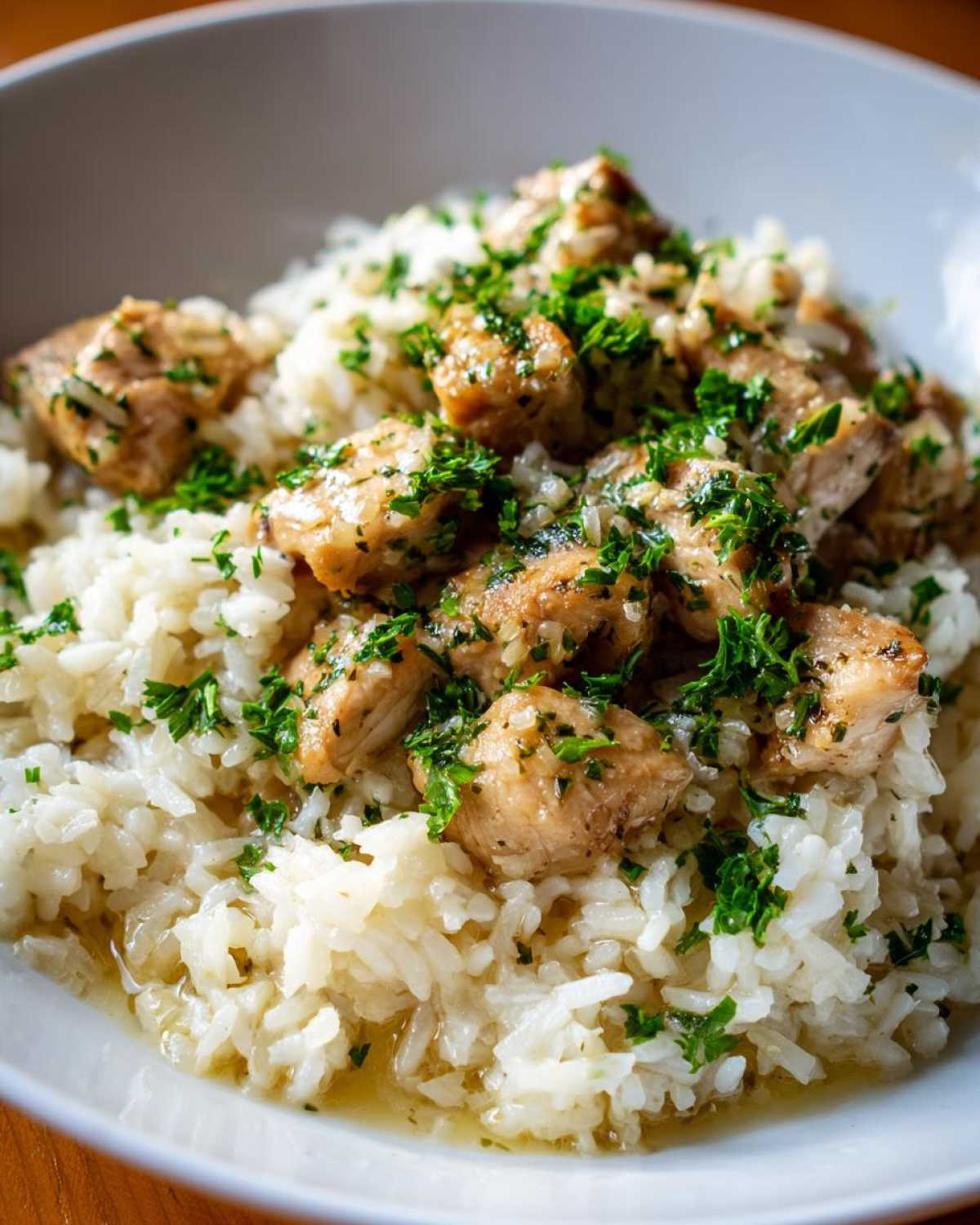 Close-up of Garlic Butter Chicken and Rice topped with fresh parsley in a light bowl.