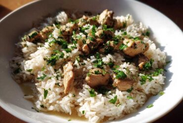 A close-up of a white bowl filled with fluffy white rice topped with chunks of chicken and fresh parsley, representing the Garlic Butter Chicken and Rice One Pot Dinner.