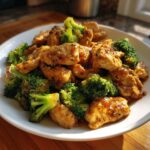 A close-up of Garlic Butter Chicken and Broccoli Stir Fry served on a white plate, glistening with sauce.