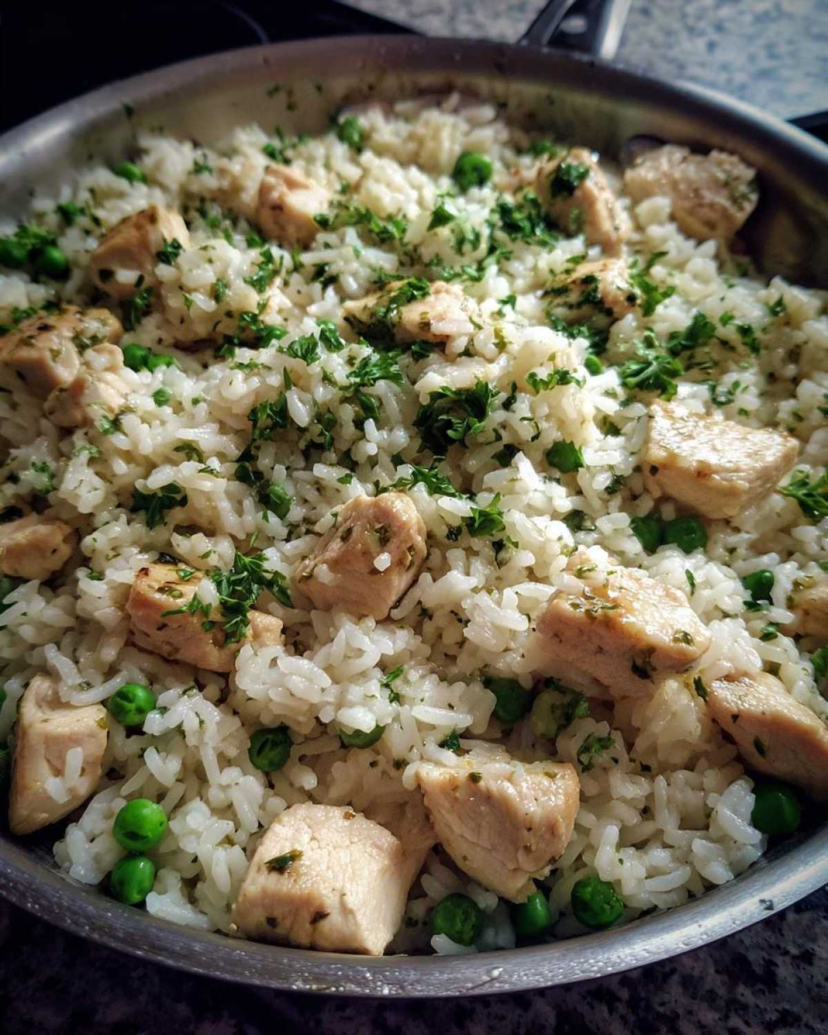 Close-up of Garlic Butter Rice with Chicken Skillet, featuring white rice, cubed chicken, peas, and parsley in a metal skillet.