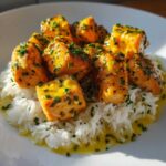 Close-up of golden Garlic Butter Salmon Bites generously coated in sauce and sprinkled with chives, served atop fluffy white rice.