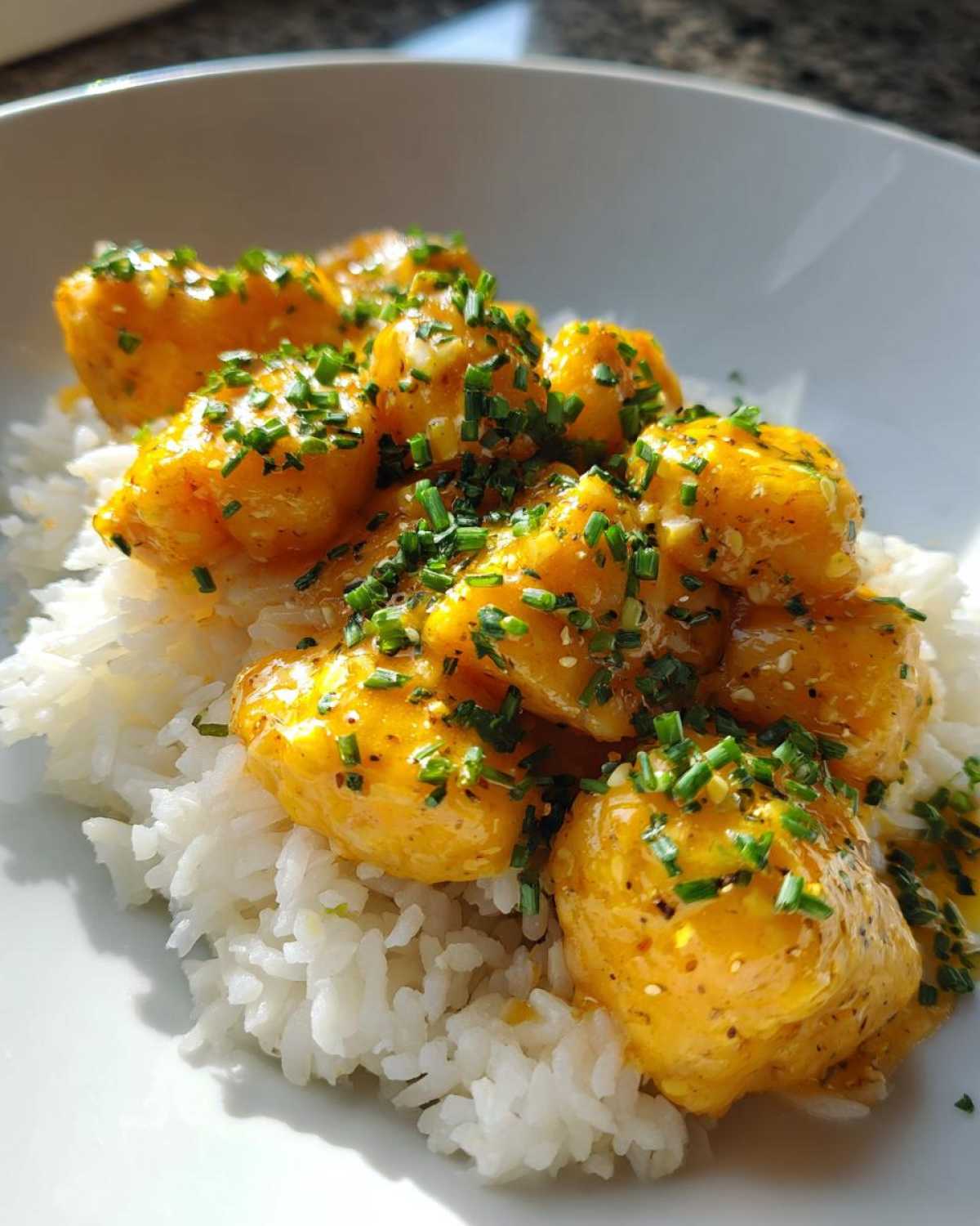 Close-up of golden Garlic Butter Salmon Bites coated in sauce and topped with chives over a bed of white rice.