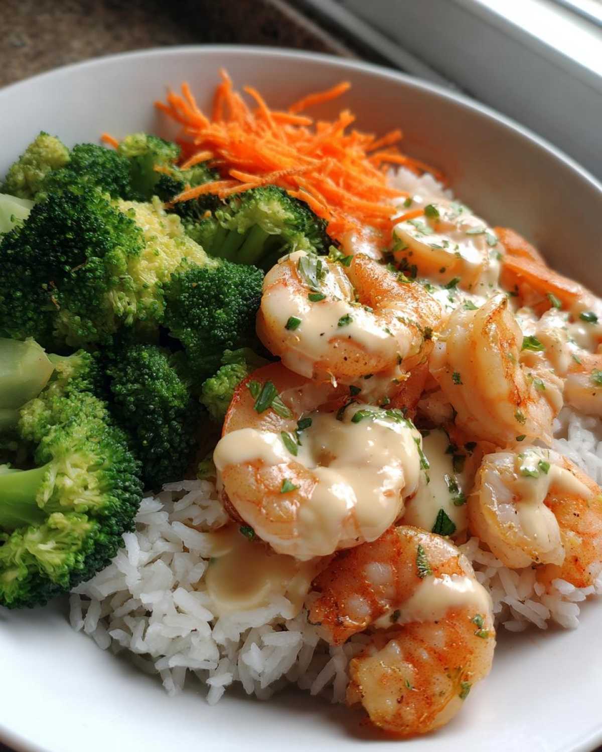 Close-up of a Garlic Butter Shrimp Rice Bowl featuring shrimp topped with garlic sauce, served over white rice with steamed broccoli and shredded carrots.