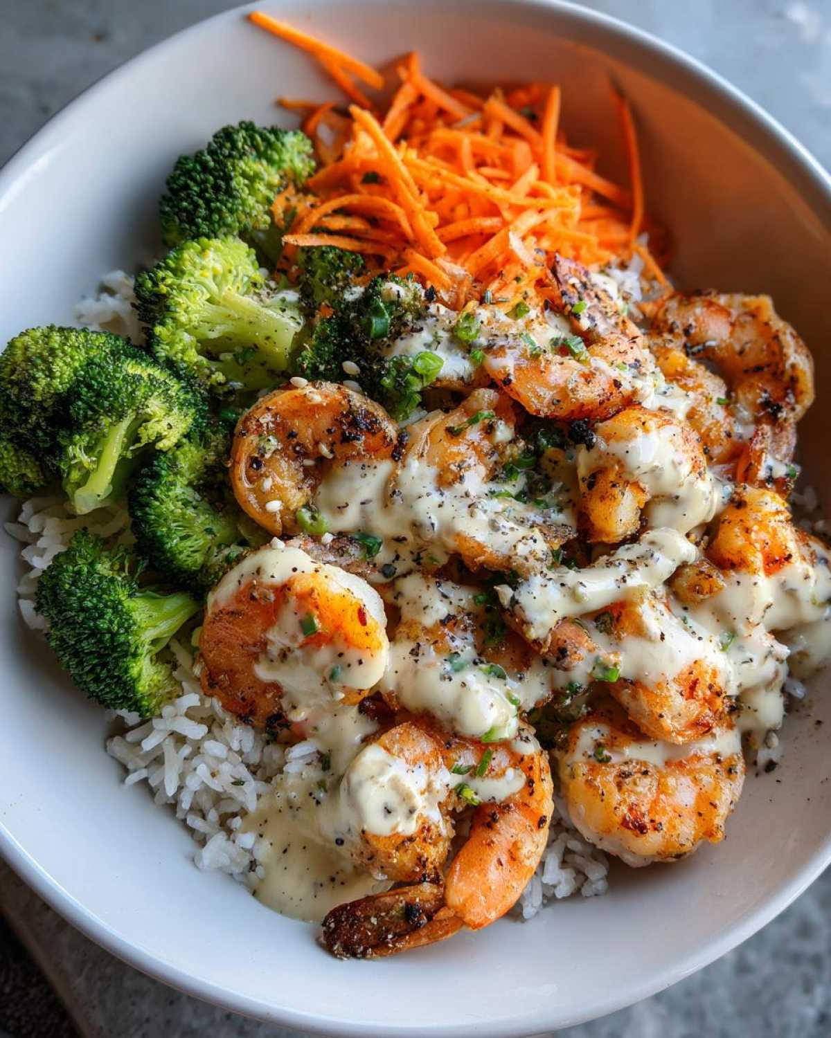 Close-up of a Garlic Butter Shrimp Rice Bowl topped with creamy garlic sauce, steamed broccoli, and shredded carrots.