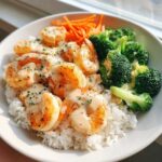 Close-up of a Garlic Butter Shrimp Rice Bowl topped with creamy garlic sauce, steamed broccoli, and shredded carrots.