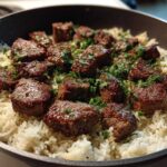 Close-up of juicy steak bites served over white rice, garnished with parsley in a skillet, featuring the Garlic Butter Steak and Rice Skillet Dinner.