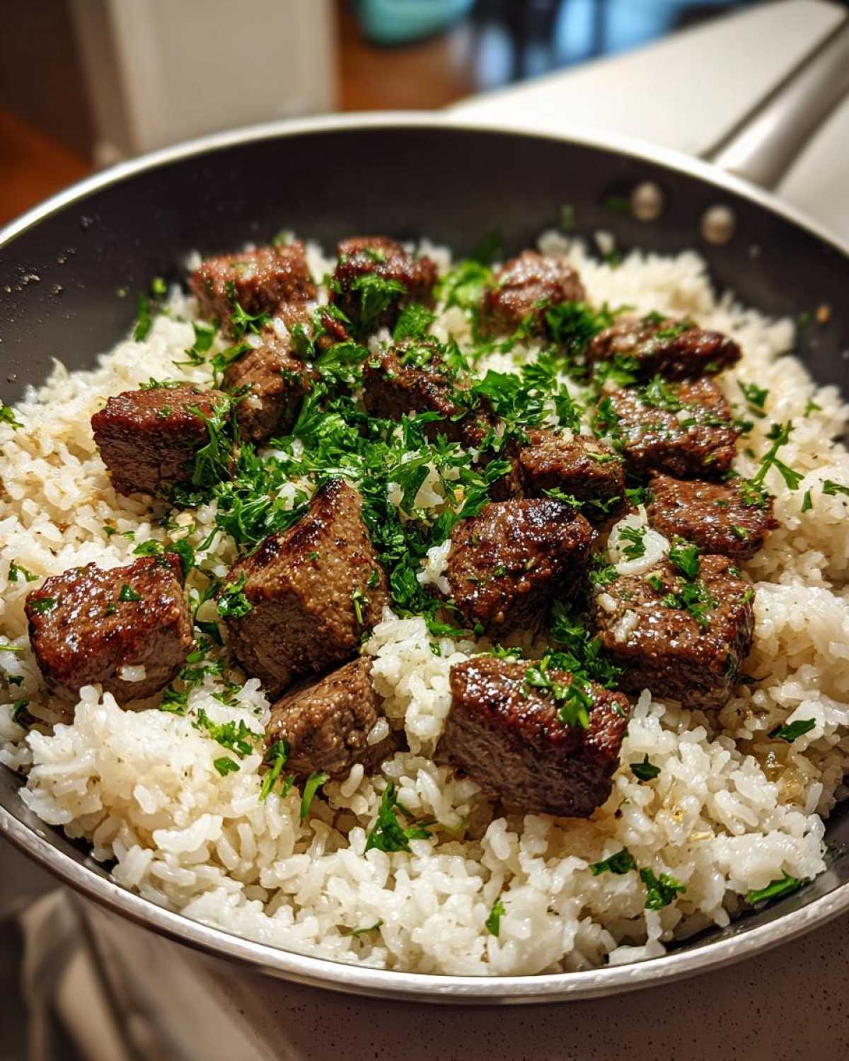Close-up of seared steak bites over white rice, garnished with fresh parsley in a skillet, showing the Garlic Butter Steak and Rice Skillet Dinner.