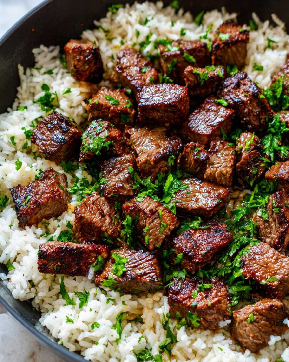 Close-up of juicy, seared steak cubes served over fluffy white rice, garnished with fresh parsley for a Garlic Butter Steak and Rice Skillet Dinner.