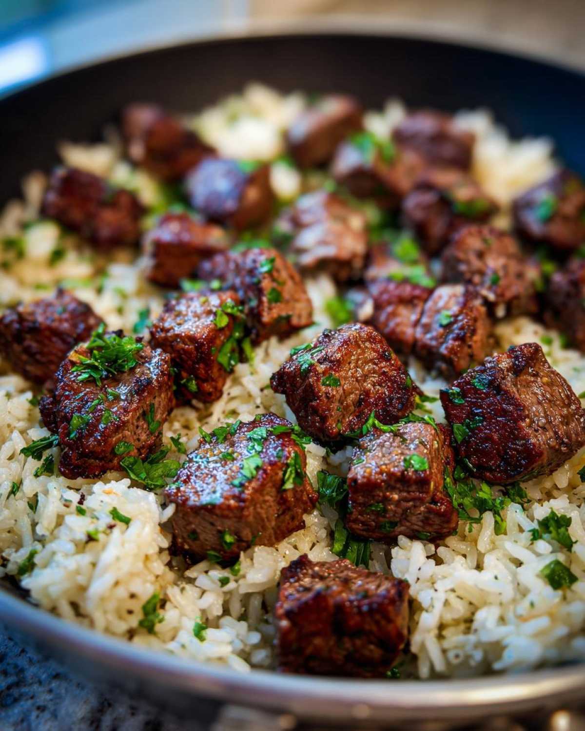Close-up of seared steak bites served over white rice in a skillet, part of a Garlic Butter Steak and Rice Skillet Dinner.