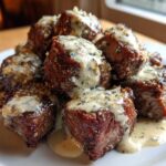 A pile of seared Garlic Butter Steak Bites generously topped with creamy garlic sauce on a white plate.