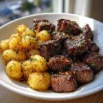 A white bowl filled with glistening Garlic Butter Steak Bites and golden crispy potatoes, garnished with herbs.