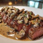 Close-up of sliced Garlic Butter Steak with Creamy Mushroom Sauce generously spooned over the medium-rare meat.