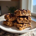 A stack of five chewy Healthy Chocolate Chip Oatmeal Bars topped with melted chocolate chips on a white plate.