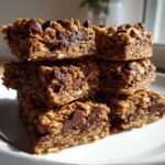 A stack of five chewy Healthy Chocolate Chip Oatmeal Bars piled on a white plate near a window.