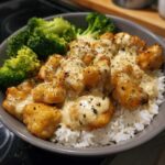 Close-up of a Honey Garlic Chicken Bowl with creamy sauce drizzled over chicken pieces served on white rice with steamed broccoli.