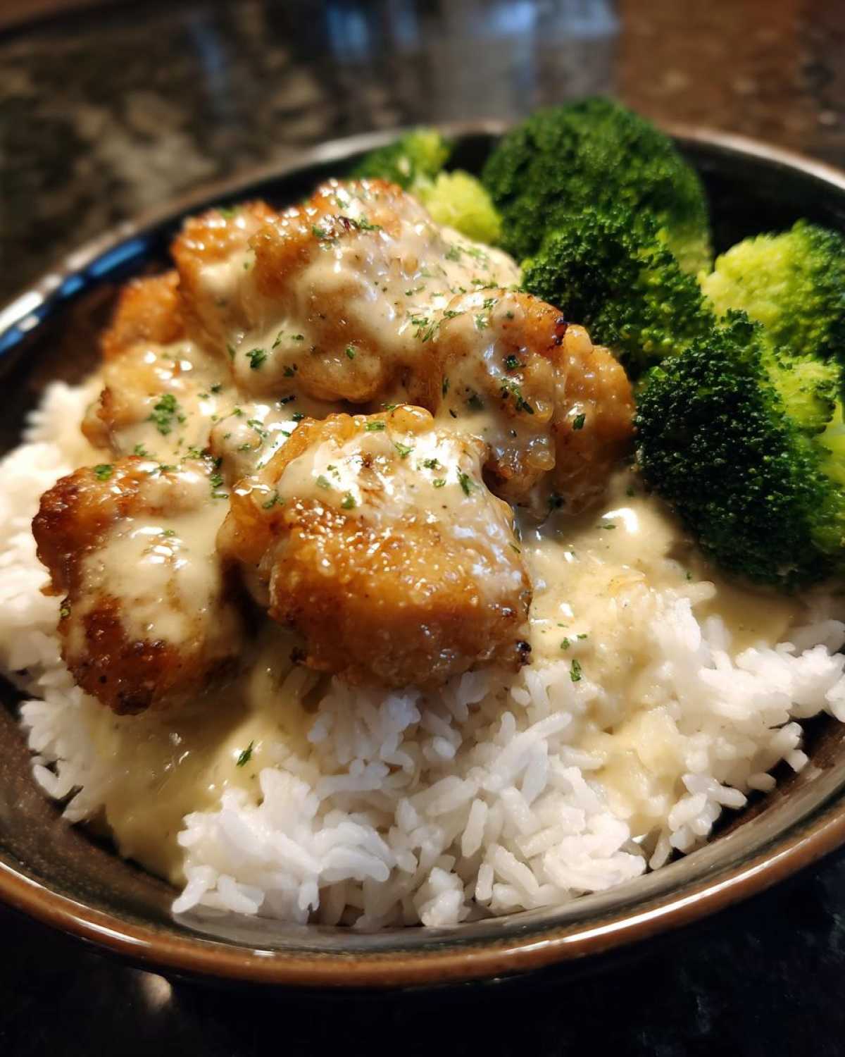 Close-up of a Honey Garlic Chicken Bowl featuring crispy chicken pieces covered in creamy sauce over white rice and steamed broccoli.