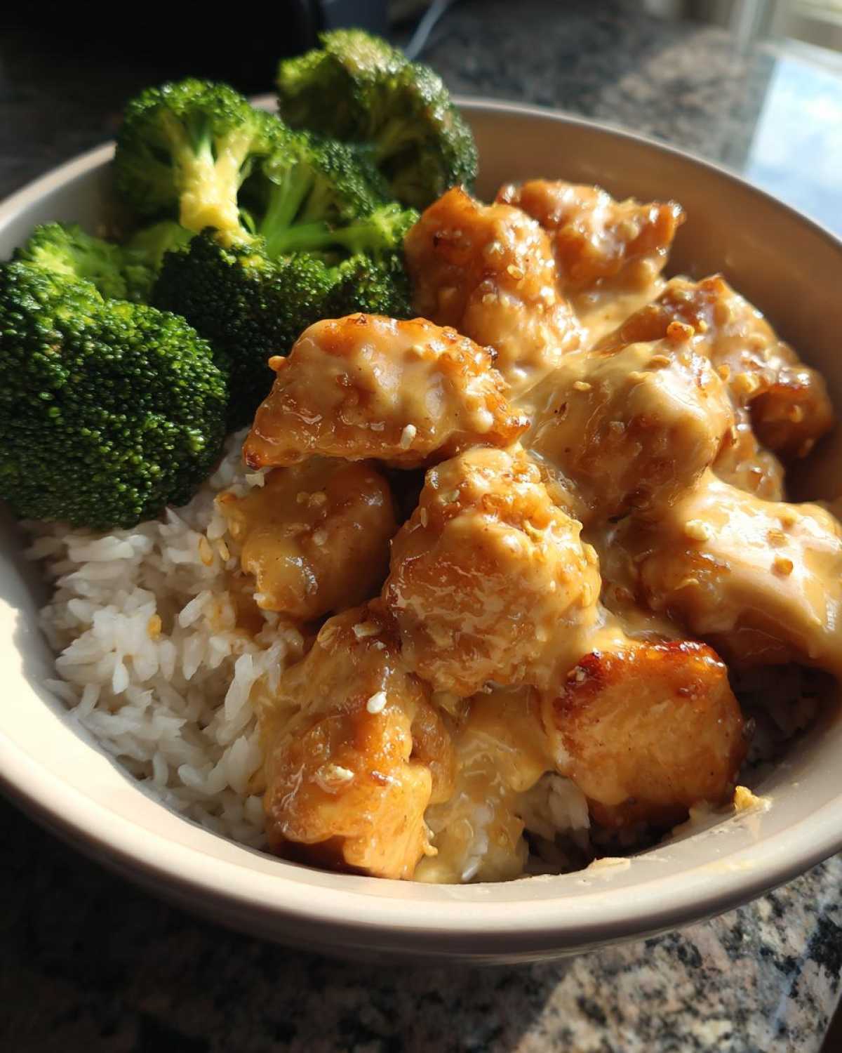 A close-up of a Honey Garlic Chicken Bowl with Creamy Sauce served over white rice with steamed broccoli florets.