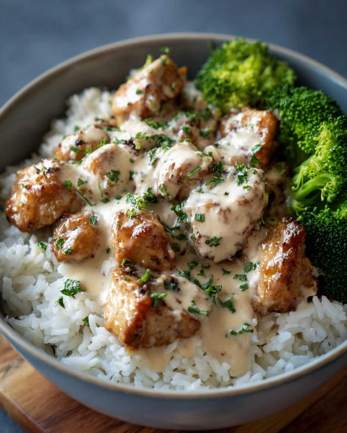 Close-up of a Honey Garlic Chicken Bowl with creamy sauce drizzled over chicken pieces on white rice and steamed broccoli.