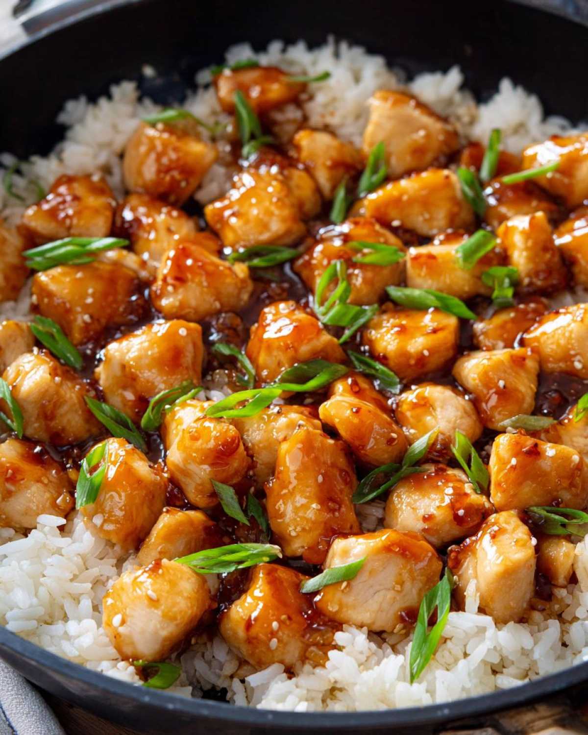 Close-up of bite-sized chicken pieces coated in glossy sauce served over white rice in a skillet, part of the Honey Garlic Chicken Skillet with Rice.