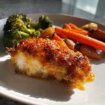 Close-up of a piece of glazed Honey Mustard Chicken Bake with crispy edges, served with roasted carrots and broccoli.