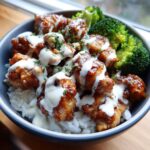 Close-up of a Honey Soy Chicken Bowl featuring glazed chicken pieces over rice, topped with white garlic sauce and steamed broccoli.
