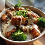 Close-up of a Honey Soy Chicken Bowl with rice, broccoli, sesame seeds, and drizzled garlic sauce.