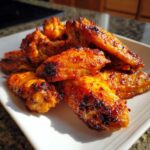 Close-up of several crispy oven baked Honey Sriracha Chicken Wings piled on a white plate.