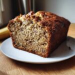 A close-up of a thick slice of Incredibly Moist Banana Bread on a white plate, showing its dense, moist crumb.