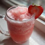 A frosty glass mug filled with Irresistible Strawberry Pina Colada Punch, garnished with a fresh strawberry slice.