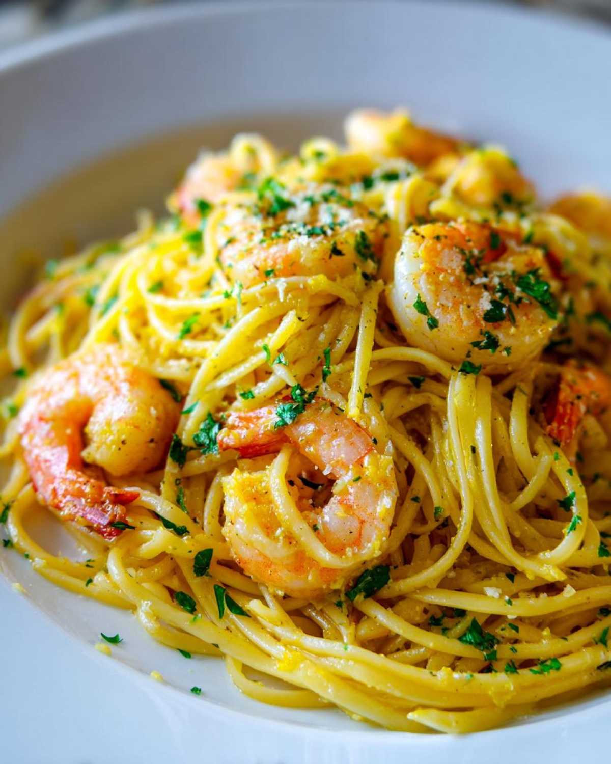 A close-up of bright, saucy Lemon Butter Shrimp Pasta topped with fresh parsley and grated cheese.