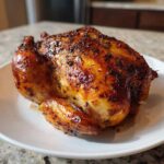 A whole, perfectly cooked Lemon Herb Roasted Chicken with incredibly crispy, glazed skin resting on a white plate.