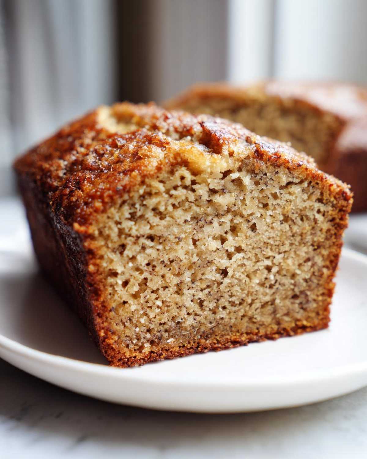 A close-up of a moist slice of homemade Banana Bread showing its tender crumb and caramelized top.